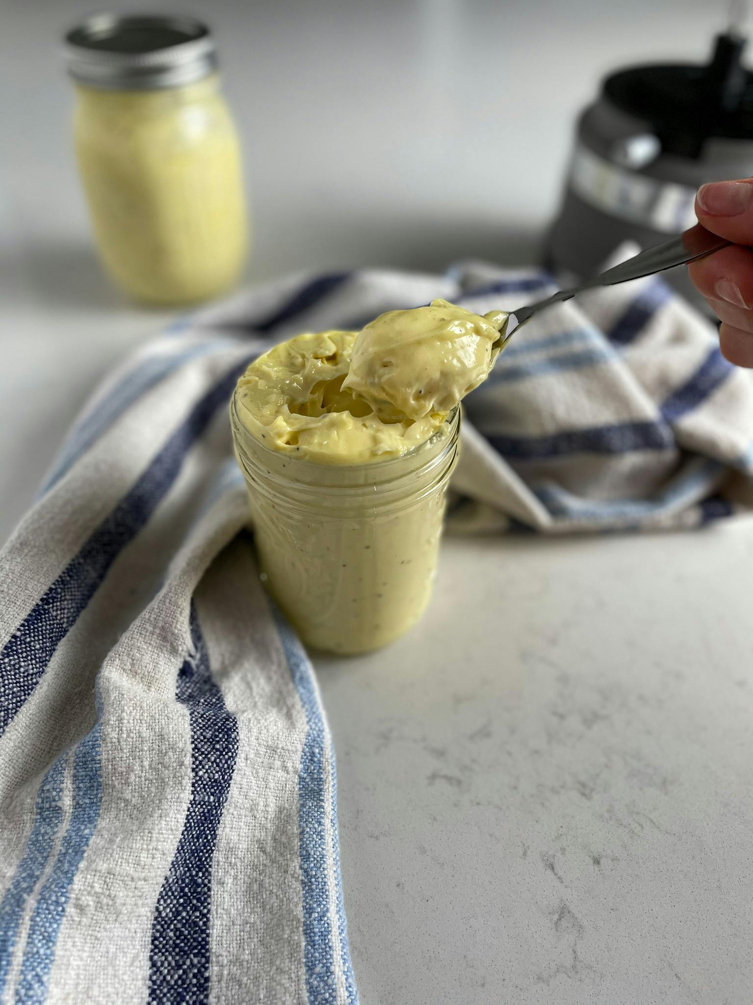 Avocado oil mayo in a glass jar being scooped out by spoon