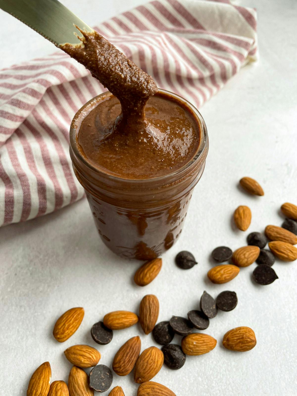 Chocolate almond butter in a jar with a knife scraping some out.