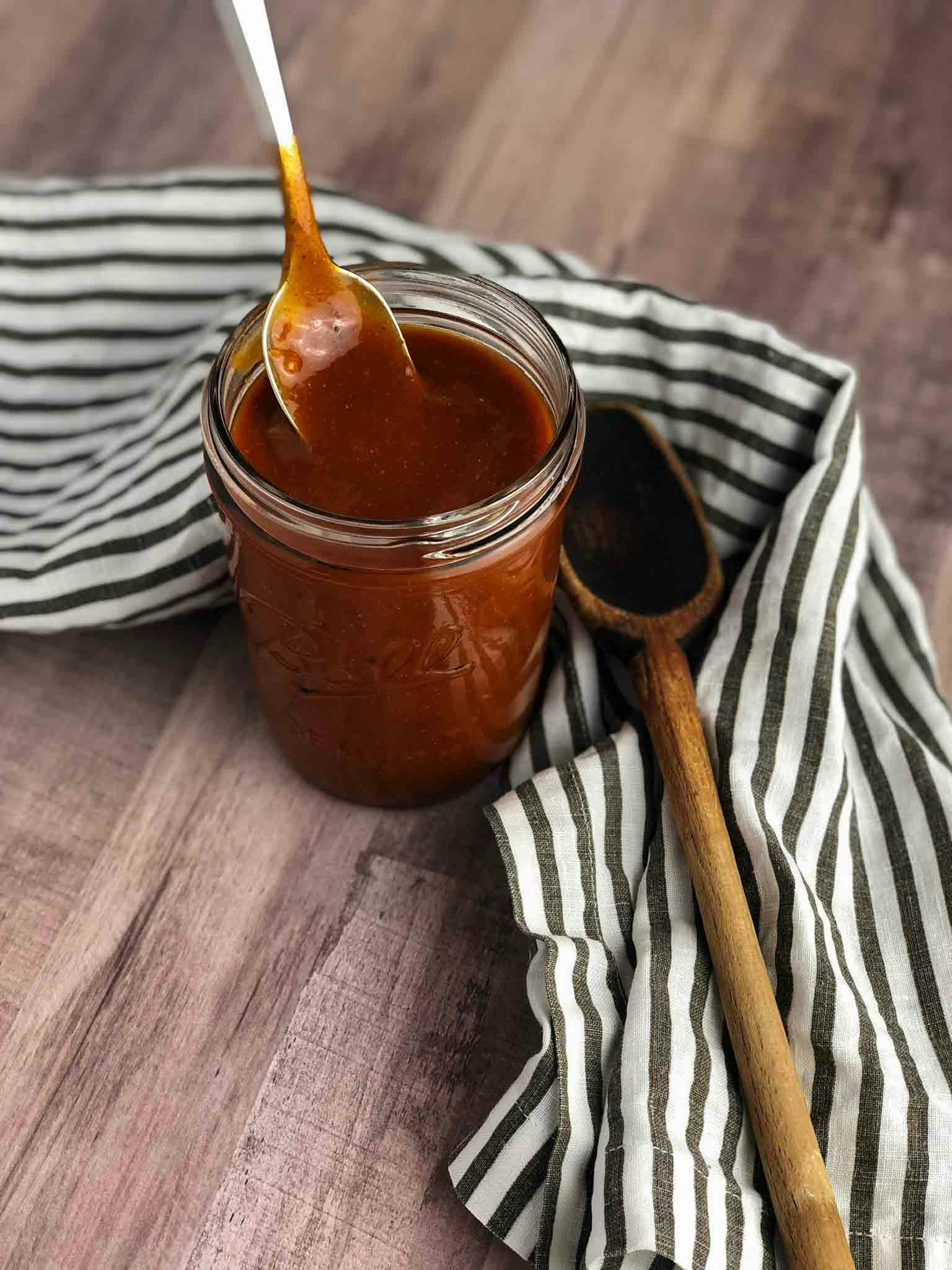 Enchilada sauce in a glass jar with a spoon dipped into it.