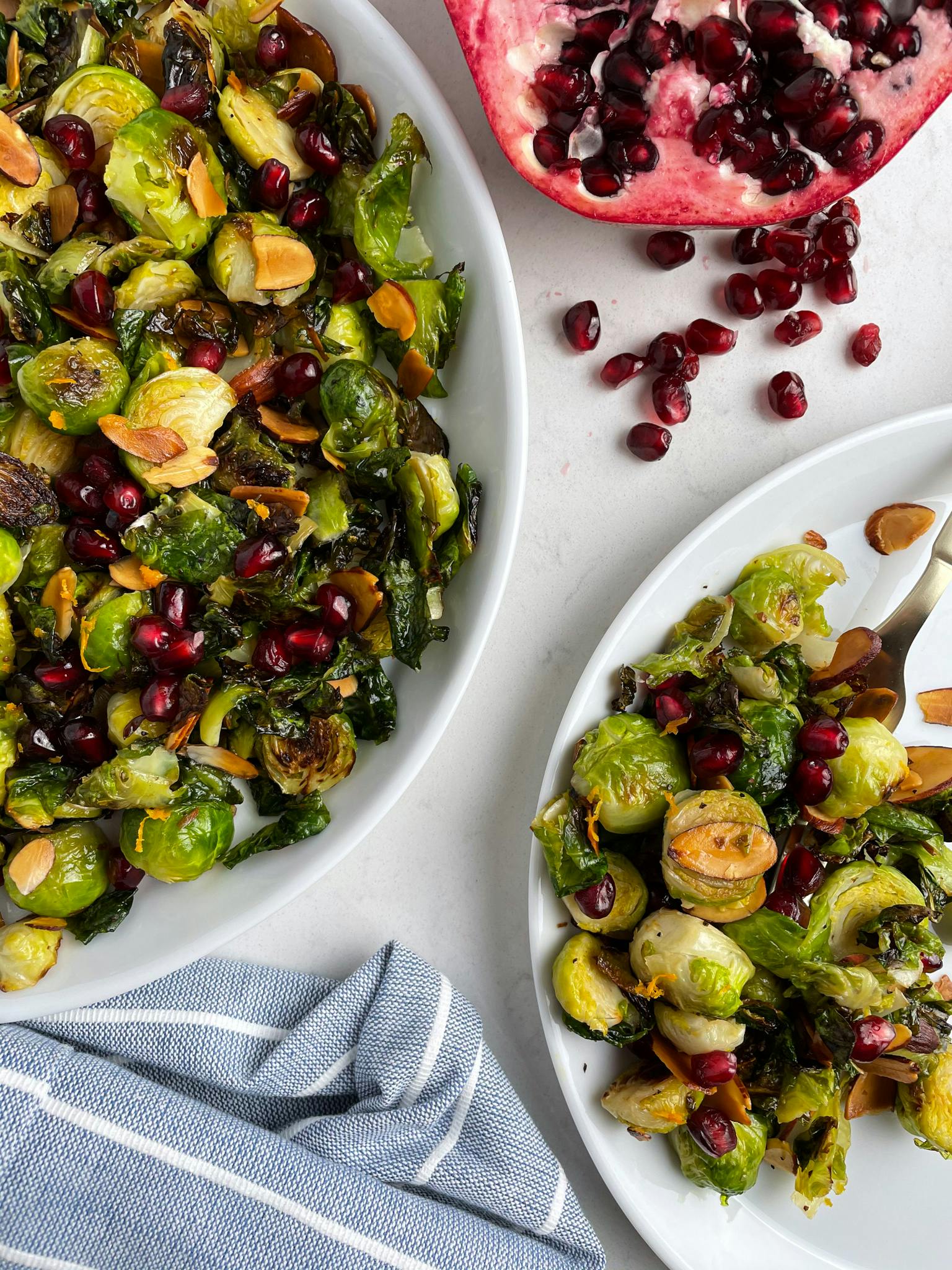 Brussels sprouts on a white plate next to a pomegranate.