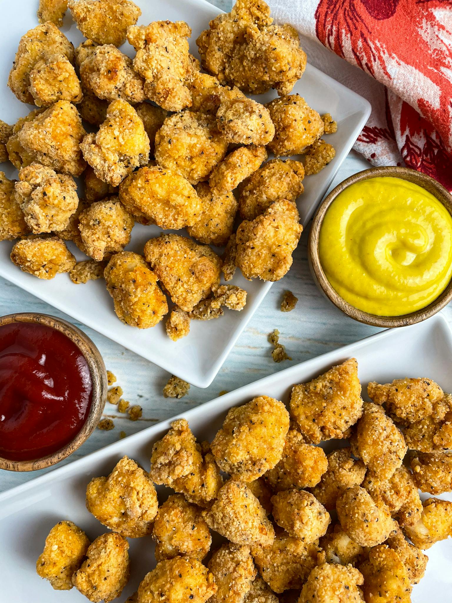Popcorn chicken on a white plate next to ketchup and mustard.